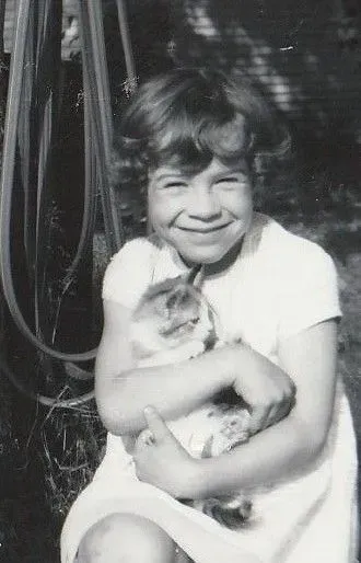 Young girl smiling, holding a tabby cat in her arms, outdoors.