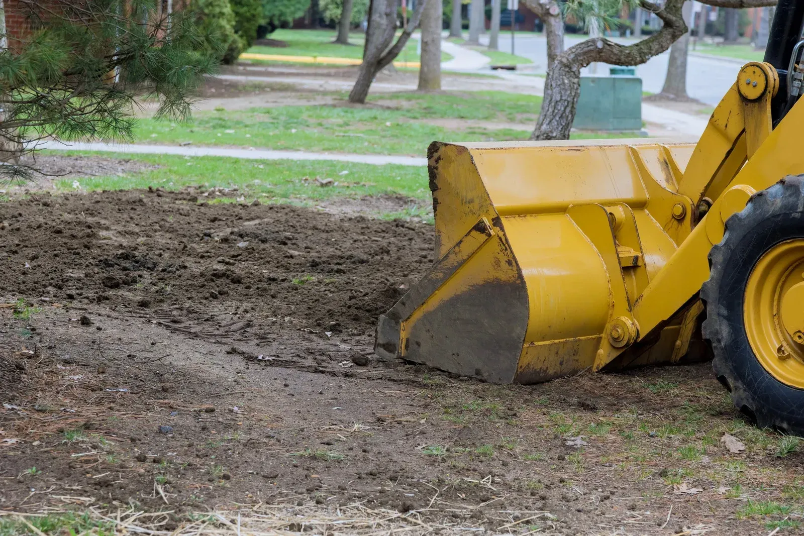 A yellow bulldozer is moving dirt in a yard.