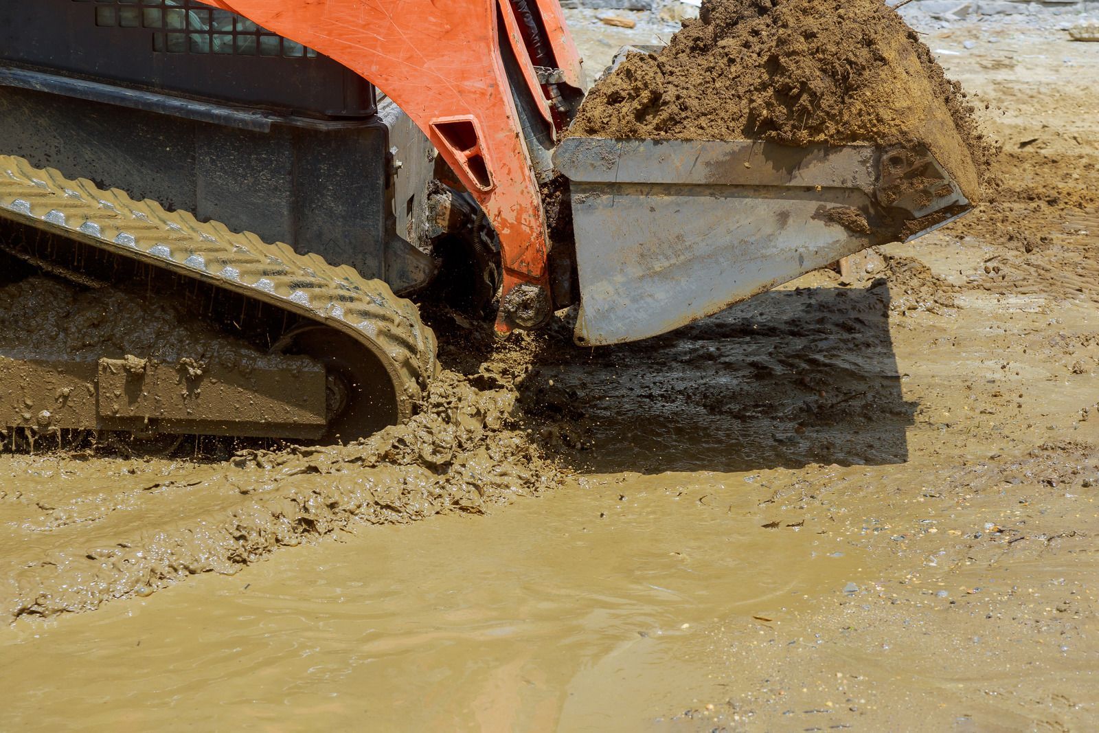 A bulldozer is scooping dirt out of a muddy field.
