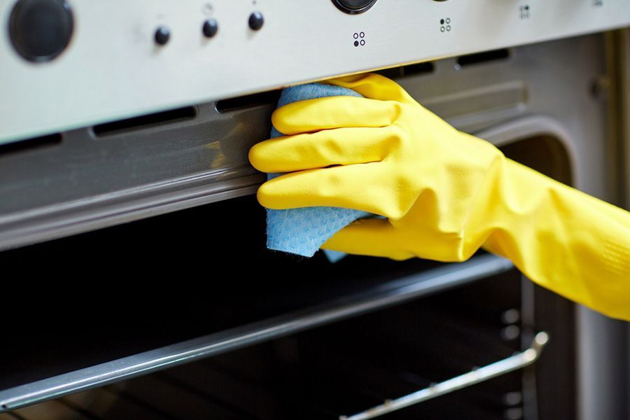 A Person Wearing Yellow Gloves Is Cleaning An Oven With A Cloth — TCM Carpet & Cleaning In Koongal, QLD