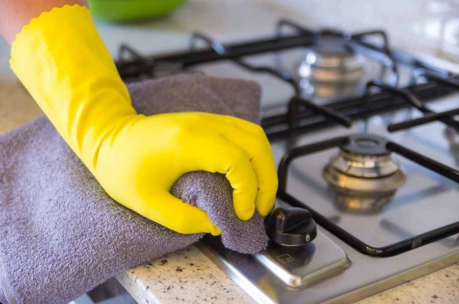 A Person Wearing Yellow Gloves Is Cleaning A Stove Top With A Towel — TCM Carpet & Cleaning In Koongal, QLD