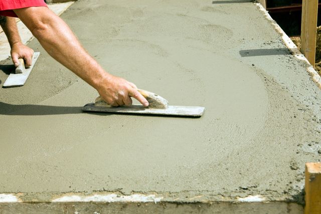 A man is using a trowel to spread concrete on a sidewalk.