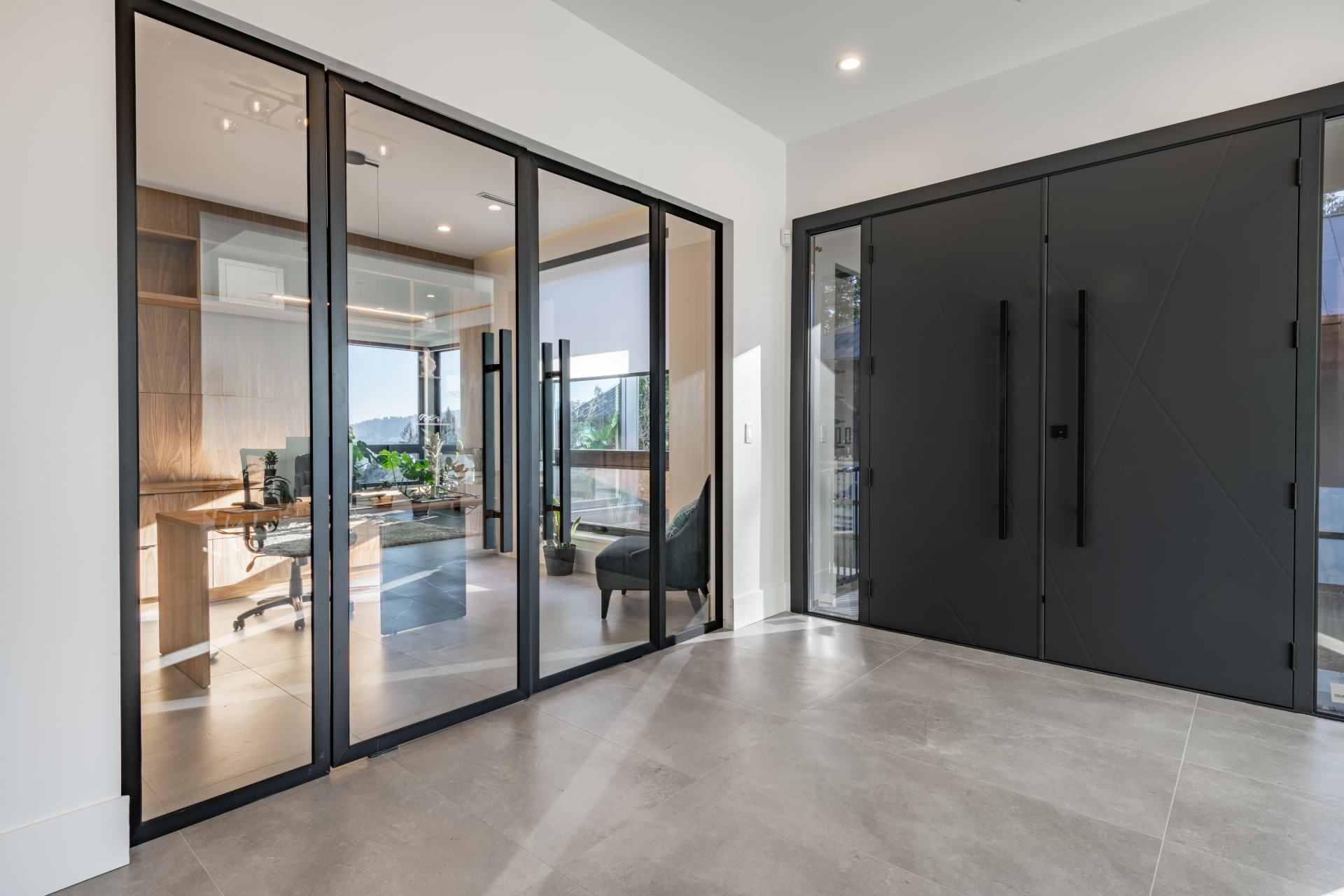 Modern entryway with glass-walled office; gray doors and floors; sunny interior with desk.