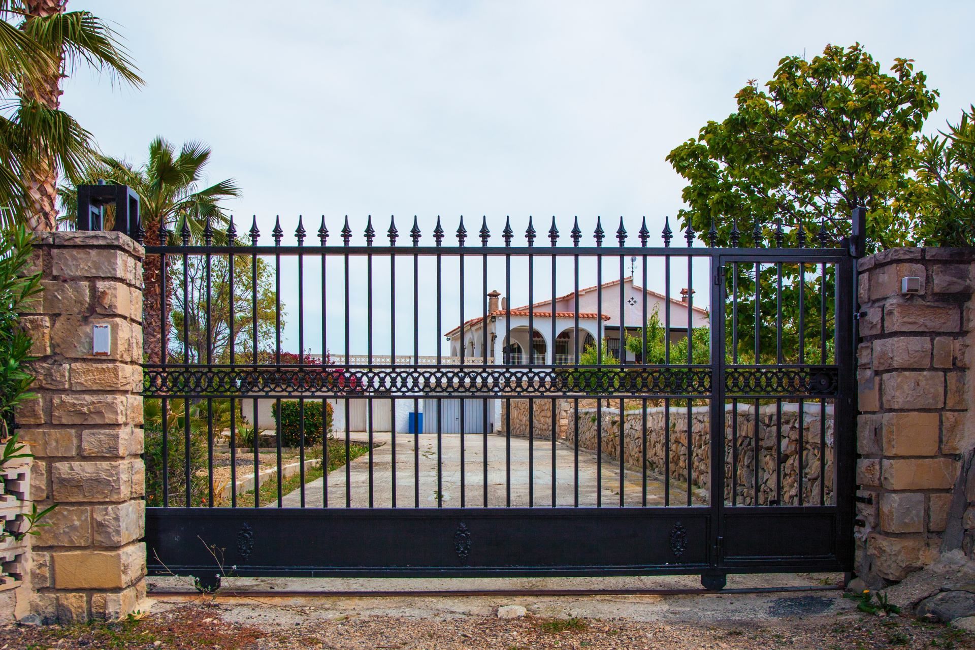 Black wrought iron gate guarding a house; pillars of stone on either side.