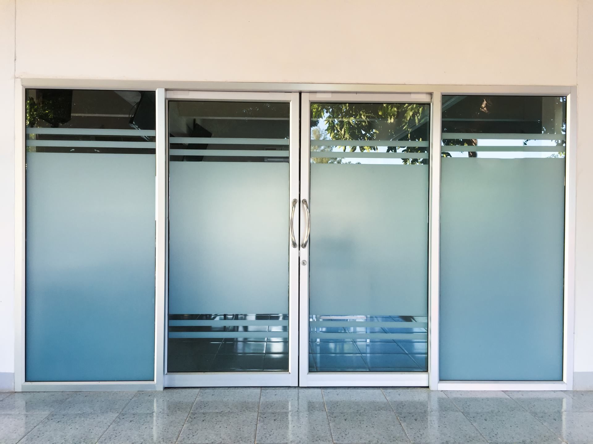 Glass sliding doors with frosted upper and lower panels. Silver frames, white building exterior, light floor.