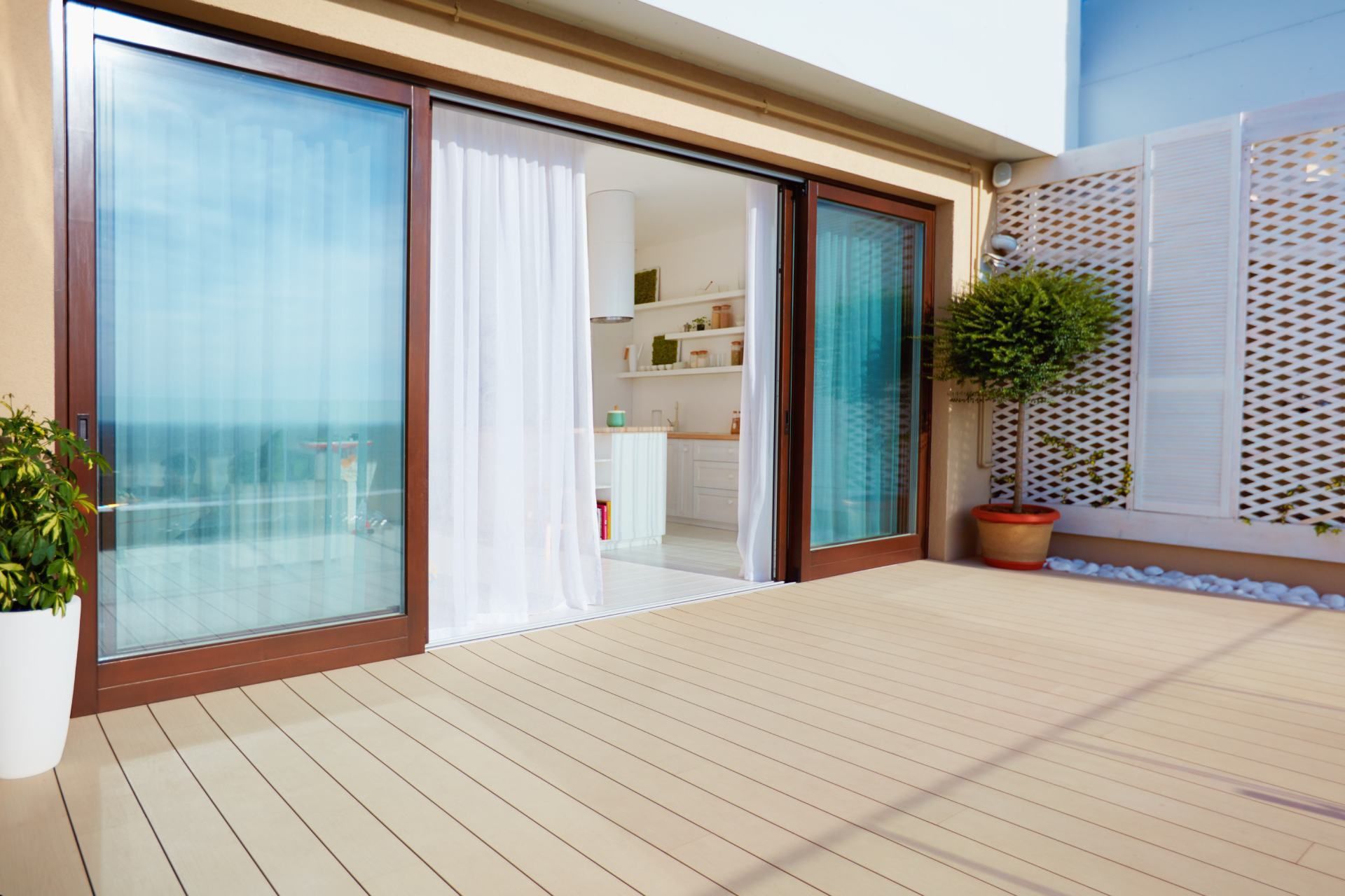 Patio with sliding glass doors, a deck, and white curtains, leading to a kitchen.
