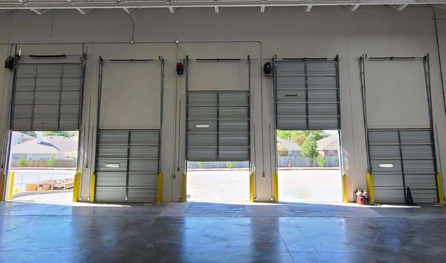 Empty garage with closed white door, gray floor, shelving, and a yellow bin.