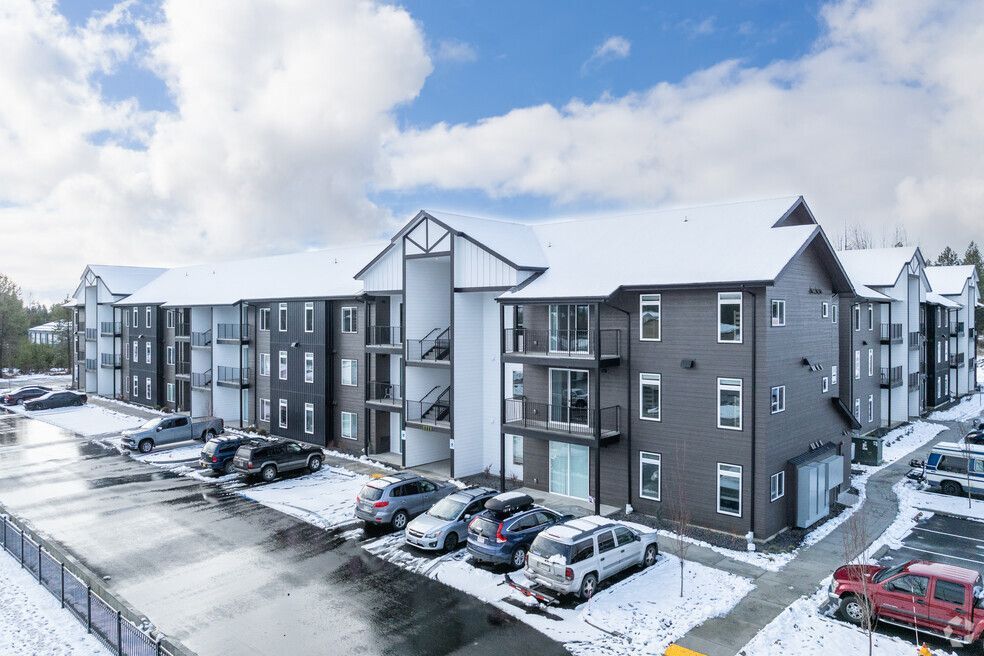 A large apartment building with snow on the roof and cars parked in front of it.