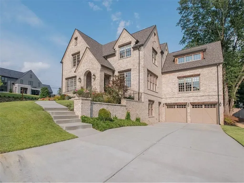 Large brick house with a concrete driveway and two-car garage. Green grass and blue sky.