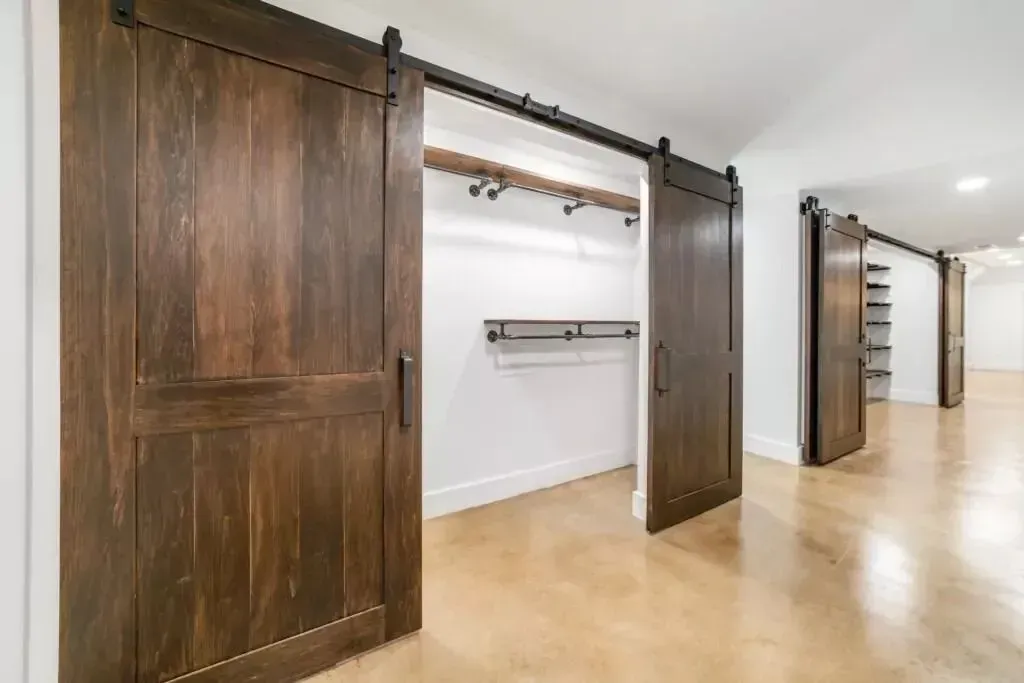 Barn doors open to reveal a closet space with shelving and clothing rod.  Dark brown wooden doors on a light brown floor.