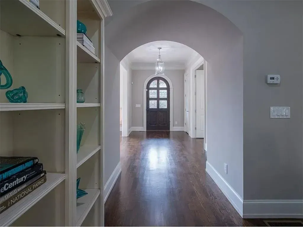 Hallway with arched doorway, bookshelf on the left, dark wood floors, gray walls.