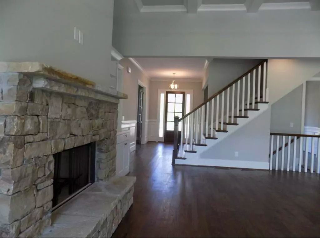 Stone fireplace in a living room, dark hardwood floors, stairs with white balusters.