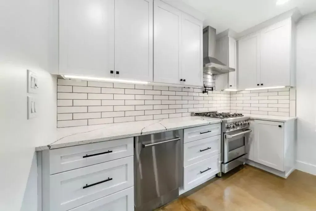 White kitchen with cabinets, stainless steel appliances, and marble countertops.