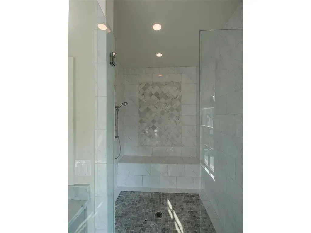 Modern shower with glass doors, white and gray tile, built-in bench, and recessed lighting.