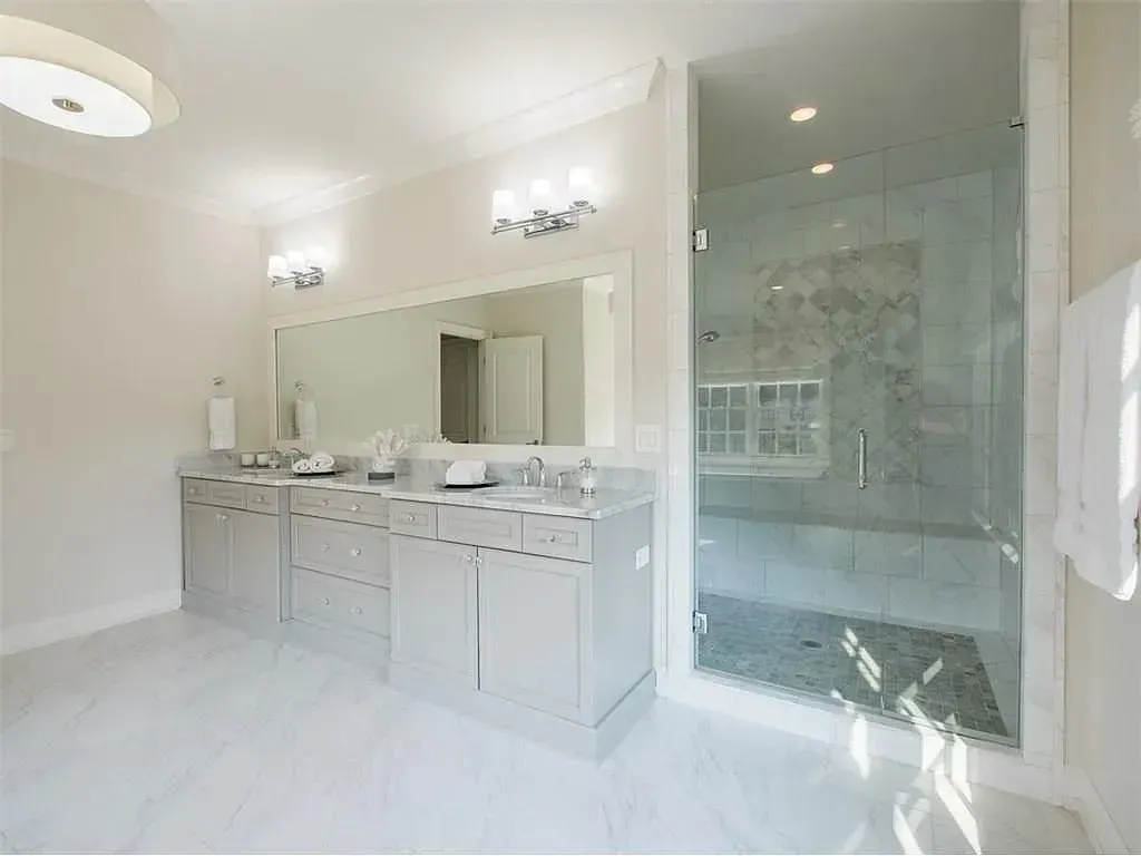 Bright, white bathroom with double vanity, large mirror, and glass shower enclosure.