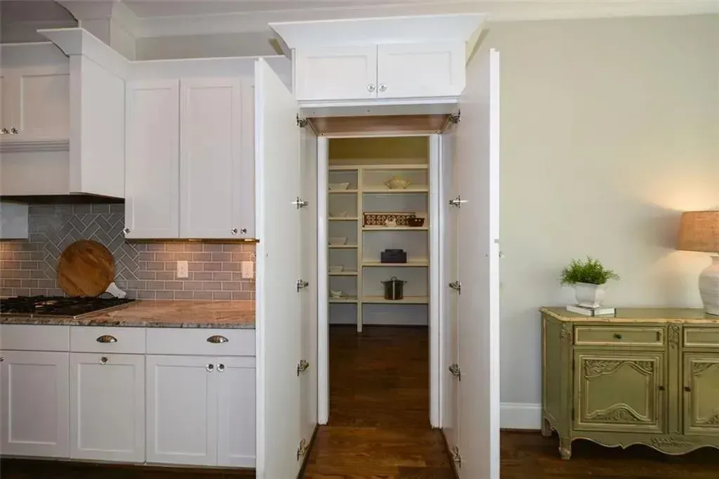 White kitchen pantry concealed by two tall, white, hinged doors, wooden floors, and a cabinet above.