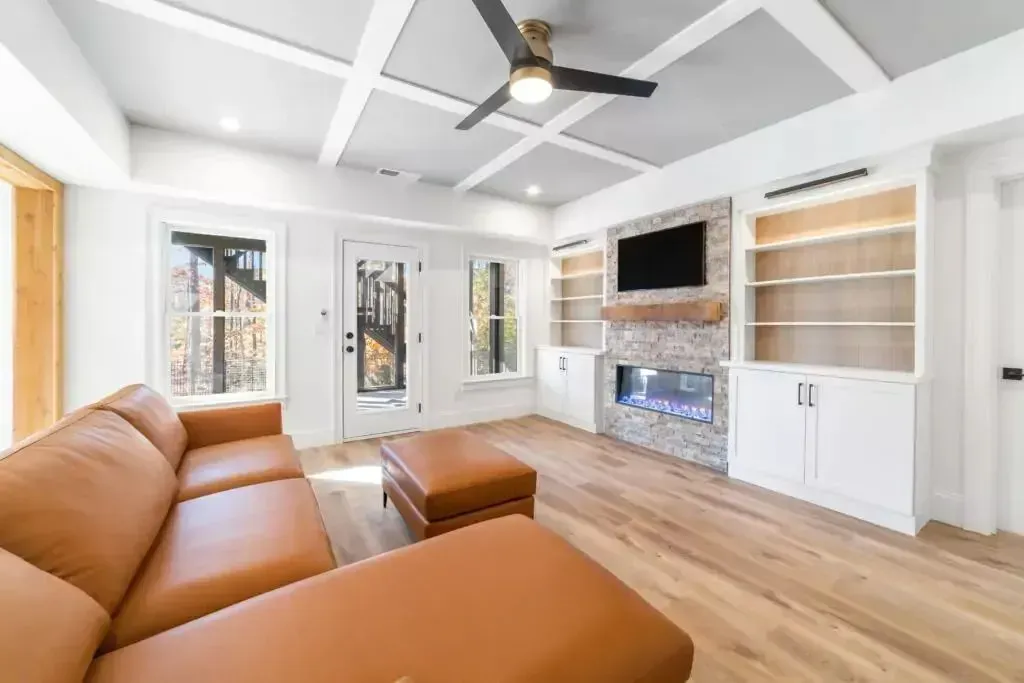 Cozy living room with brown sectional, fireplace, built-in shelving, and coffered ceiling.