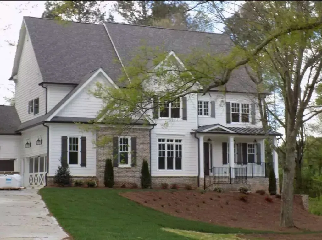 Two-story white house with dark shutters, brick accents, and a front porch.