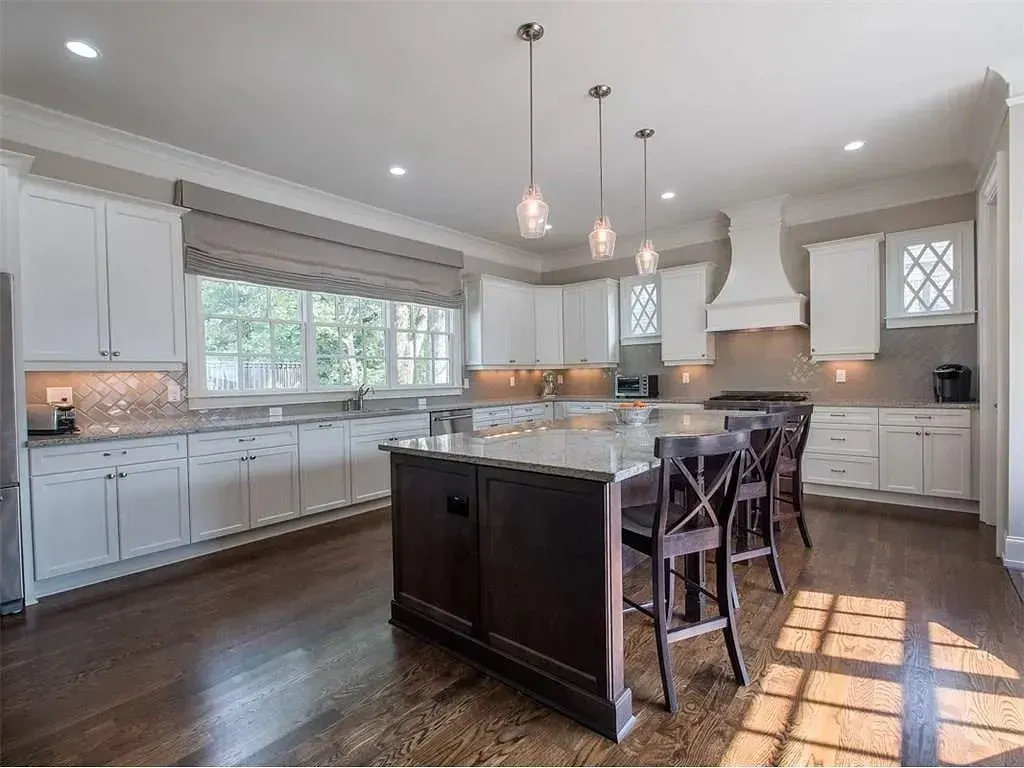 Modern kitchen with white cabinets, dark island, pendant lights, and hardwood floors.