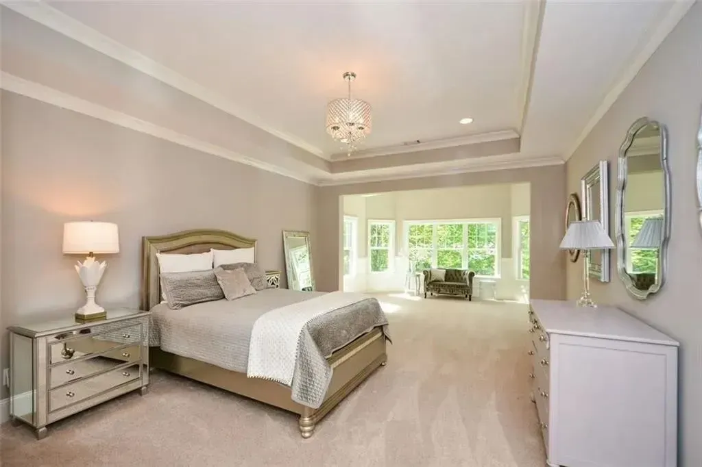 Bedroom with bed, mirrored nightstand, white dresser, and crystal chandelier.  Windows show a green, outdoor view.