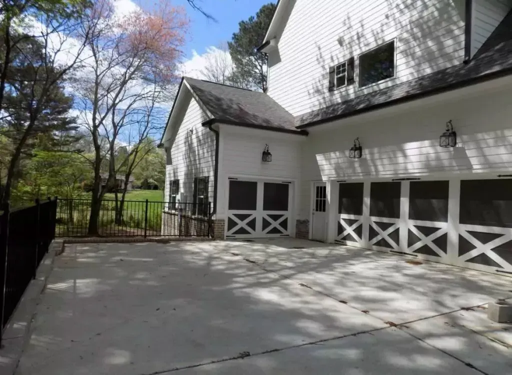 White house with three garage bays; paved driveway and black fence in yard.