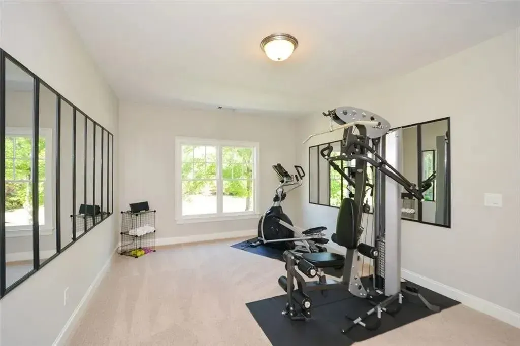 Gym with exercise equipment, mirrors, and windows; light-colored carpet and walls.