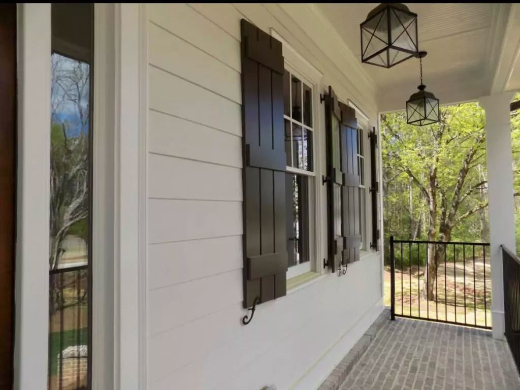 White house exterior with dark brown shutters, brick porch, and hanging lanterns.