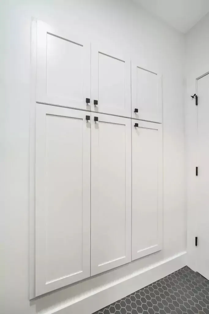 White storage cabinets with black handles against a white wall in a room with patterned floor tiles.