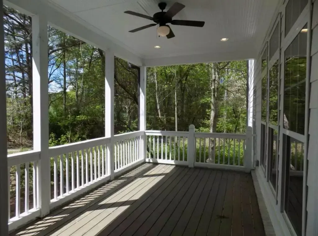 Covered porch with white railings, a ceiling fan, and a view of a wooded area.