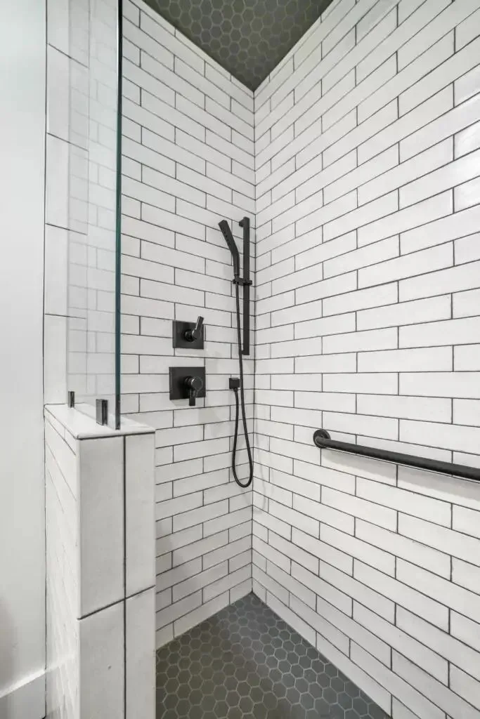 White tiled shower with black fixtures and safety grab bar.
