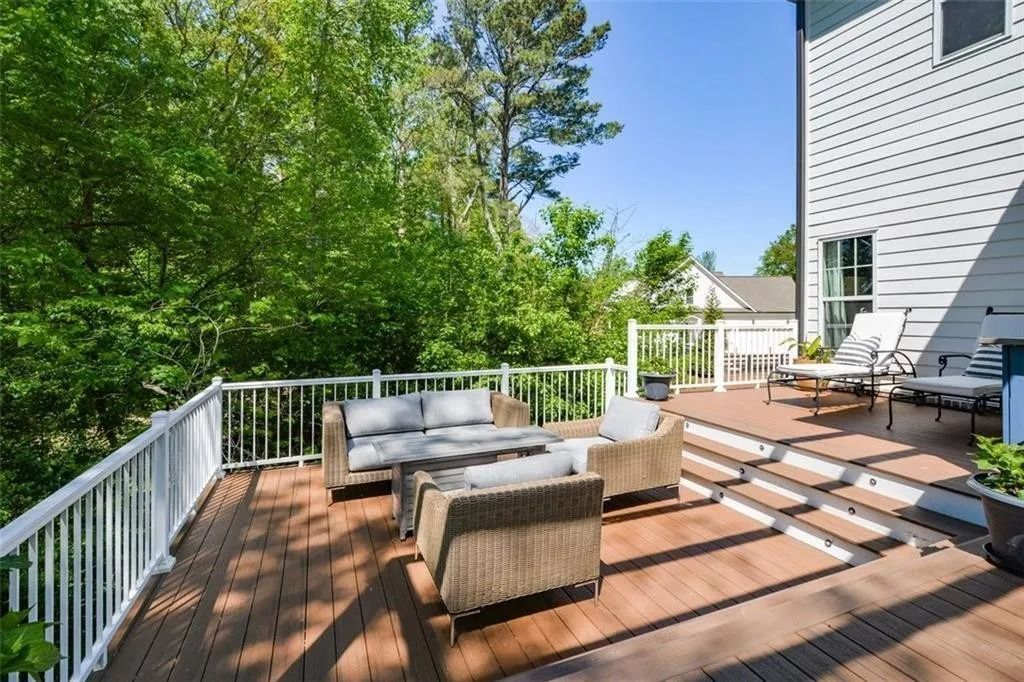 Wooden deck with patio furniture, overlooking greenery. White railing and side of a house.