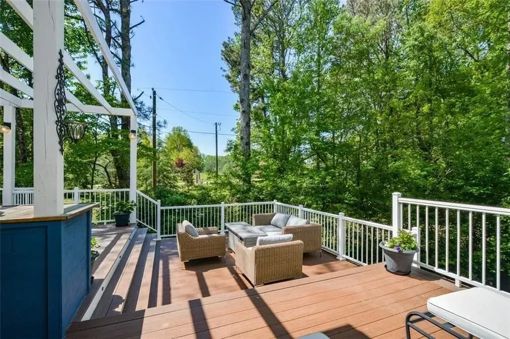 Wooden deck with outdoor furniture, overlooking a wooded area on a sunny day.