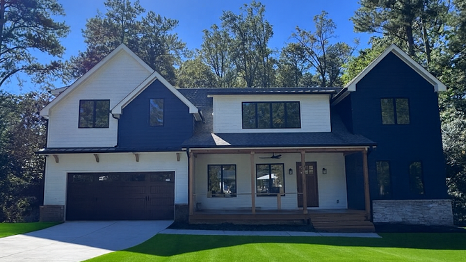 A two-story house with a white and dark blue exterior, a garage, a front porch, and surrounding trees under a blue sky.