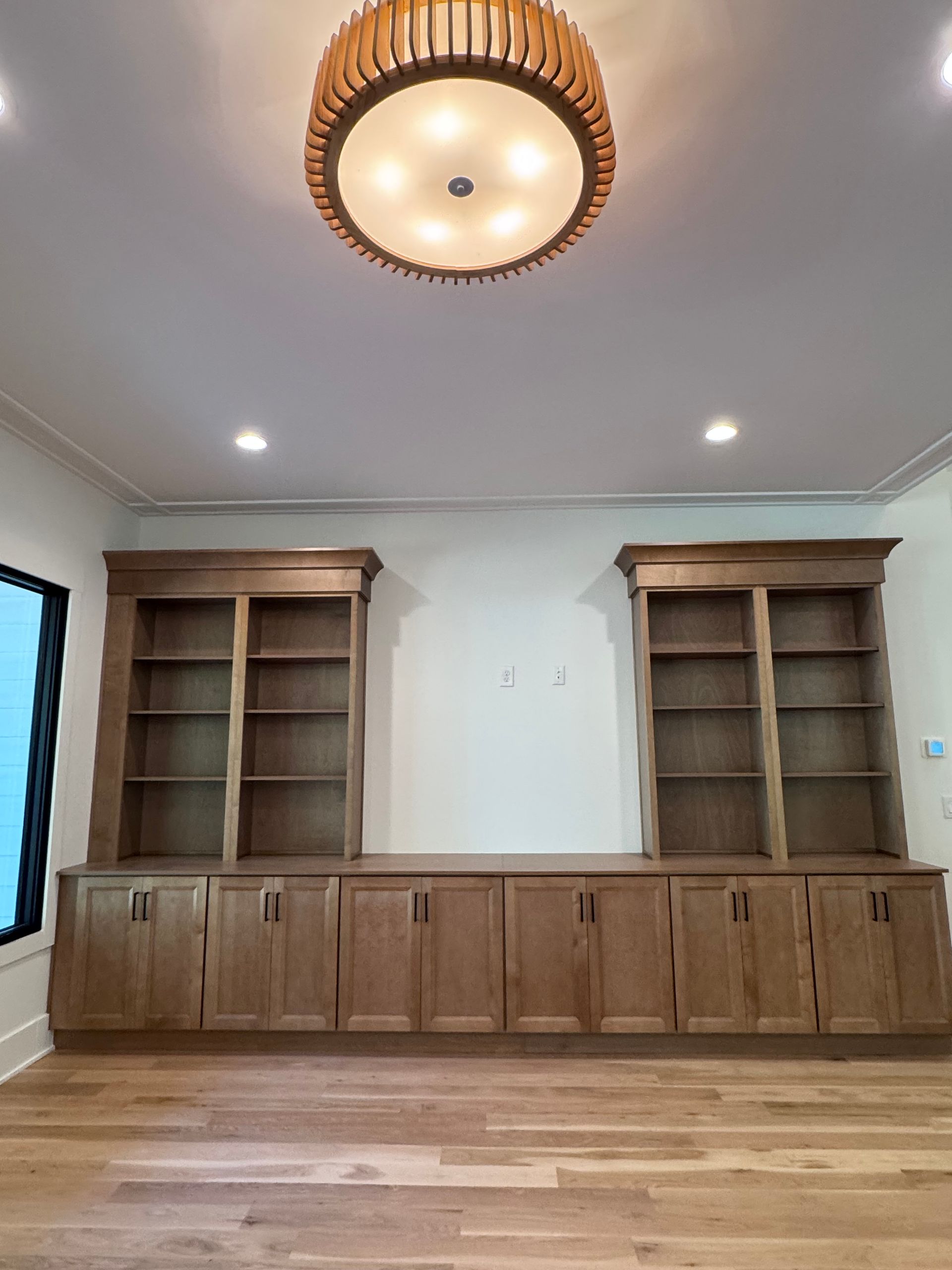 Built-in wooden bookshelves and cabinets on a light-wood floor, under a round light fixture.
