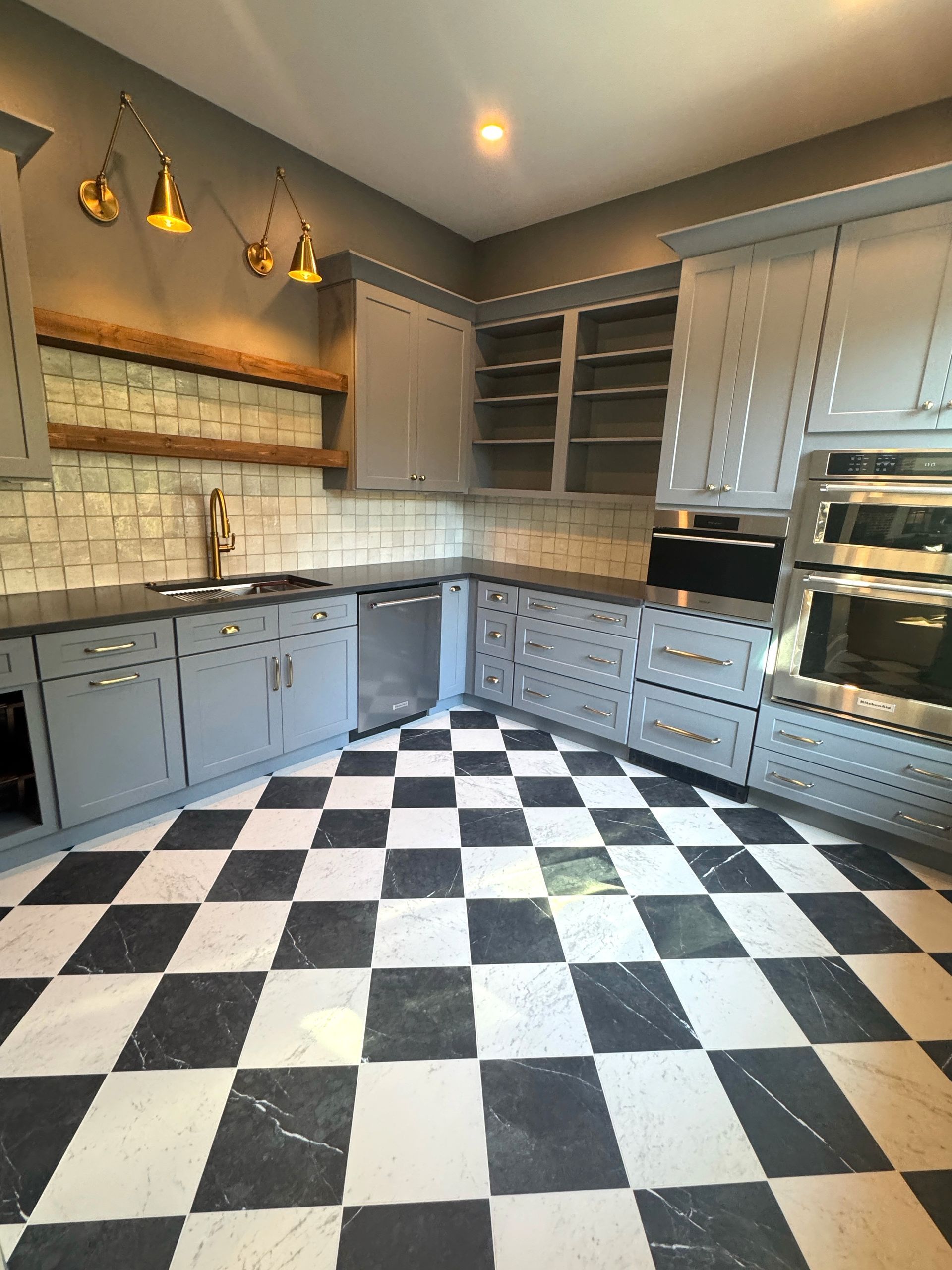 A modern kitchen with gray cabinets, black countertops, and black and white checkered floor.