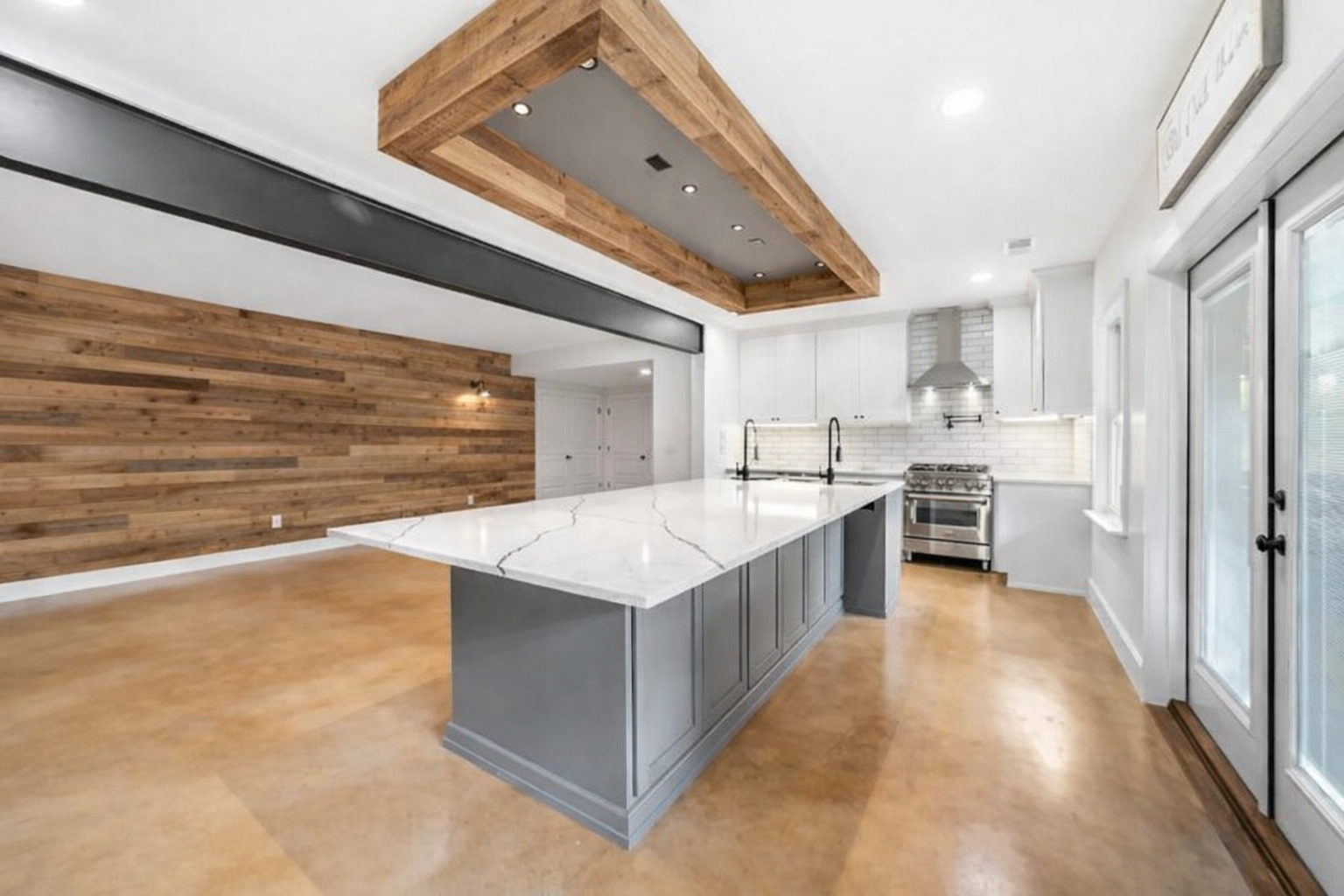 Modern kitchen with wood accent wall, gray island with marble countertop, and wood beam hood.