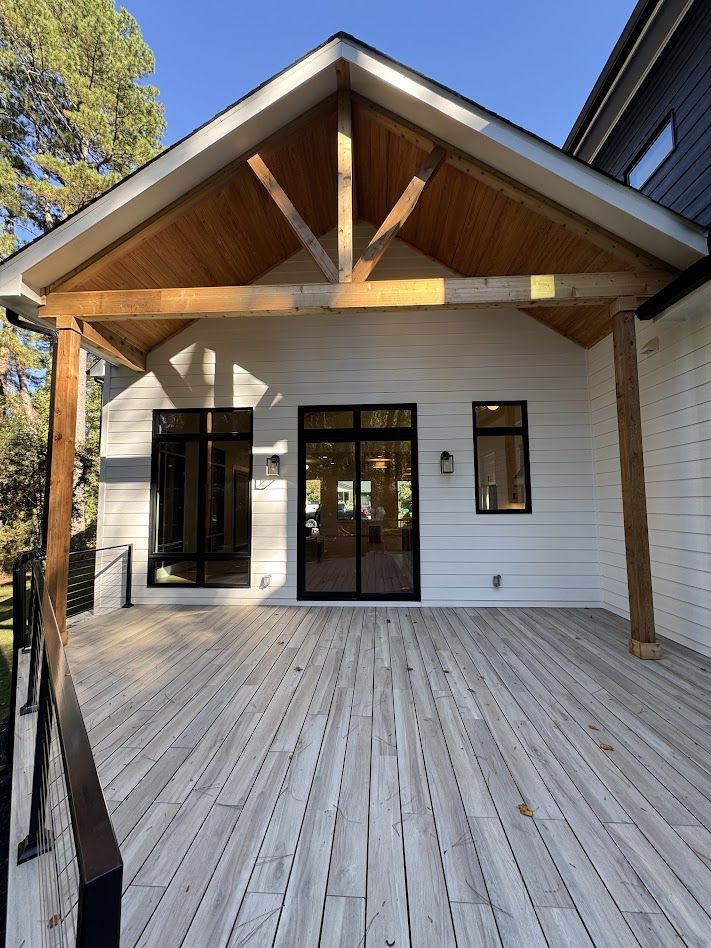 Wooden-decked porch with white siding, black-framed glass doors and windows, and a wooden beam roof.