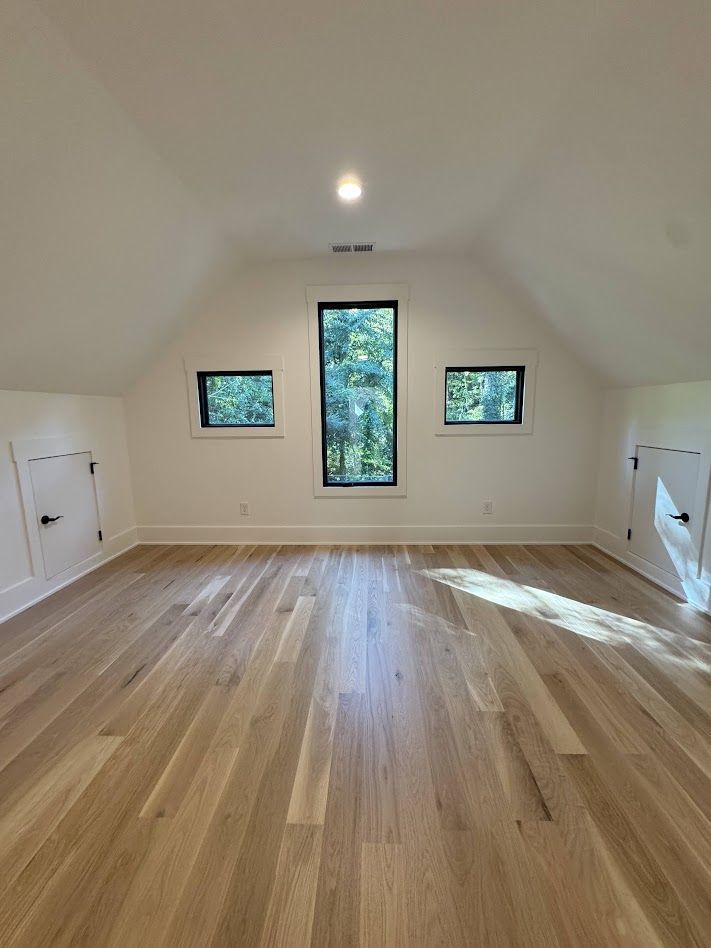 Empty room with light wood floors, white walls, and three windows with dark frames.