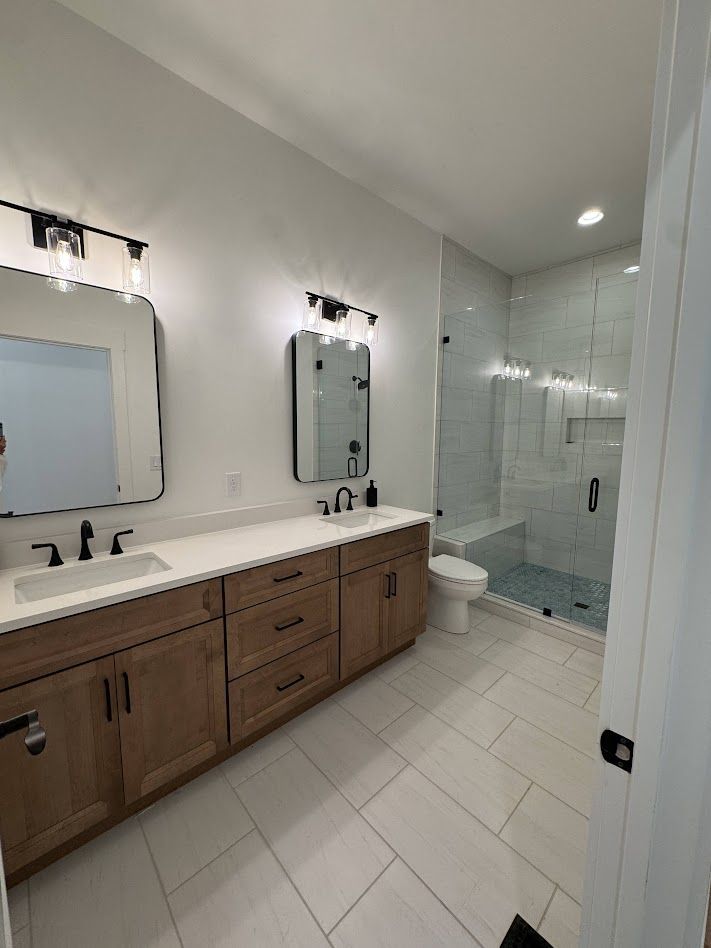 Bathroom with a wooden vanity, two mirrors, a shower, and white tile.