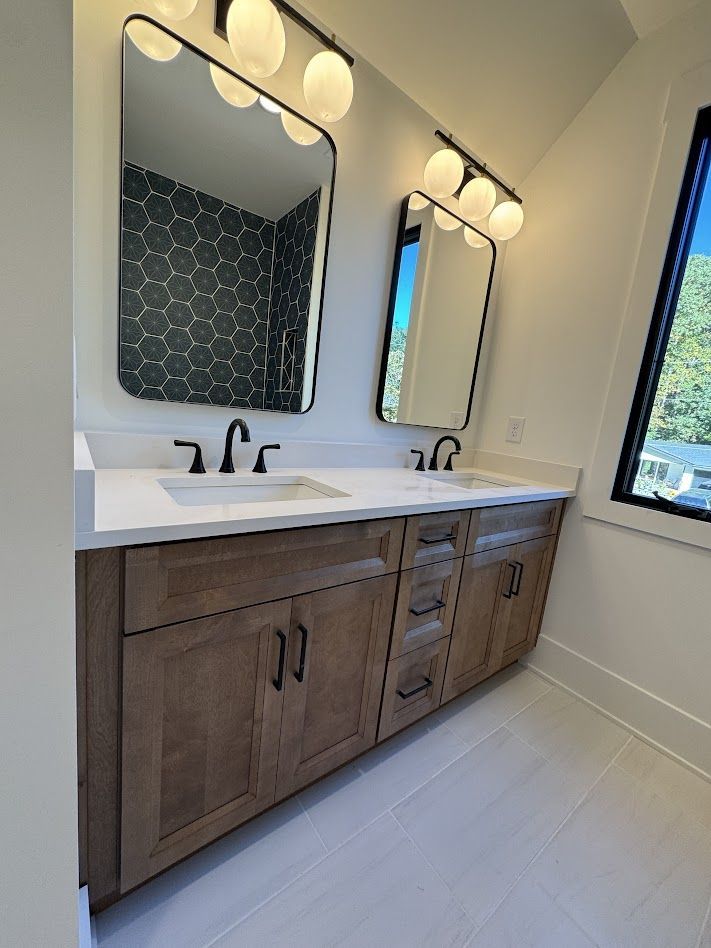 Bathroom vanity with two mirrors, brown cabinets, white countertop, and gray tiled floor.