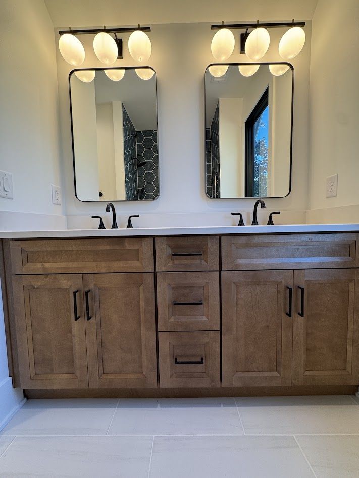 Bathroom vanity with two mirrors, lights, and wooden cabinets. Black fixtures and white countertop.