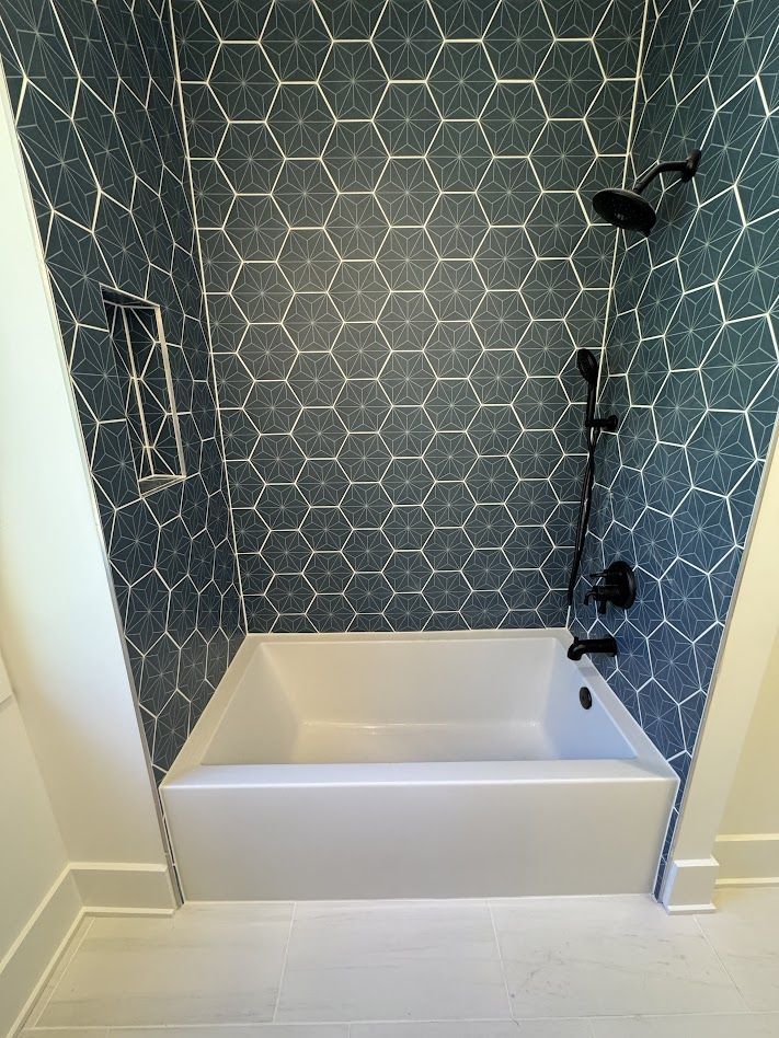 Blue hexagon-tiled shower surround with white tub and black fixtures; recessed shelf.