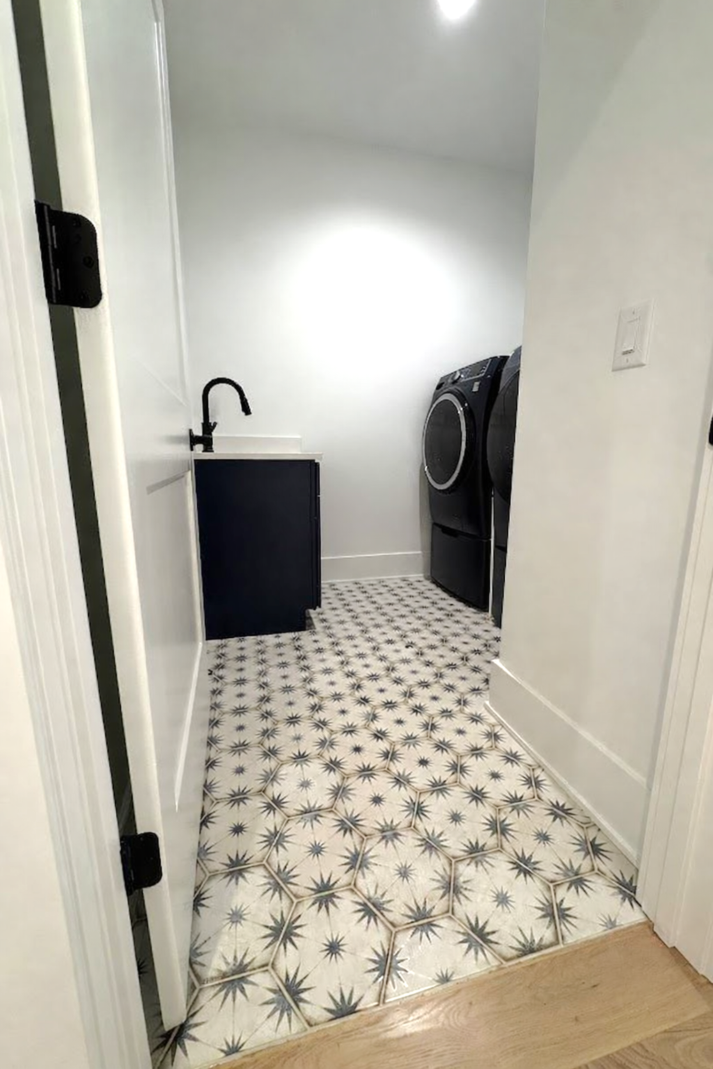 Laundry room with star-patterned tile floor, navy blue cabinet, black faucet, and black washer/dryer.