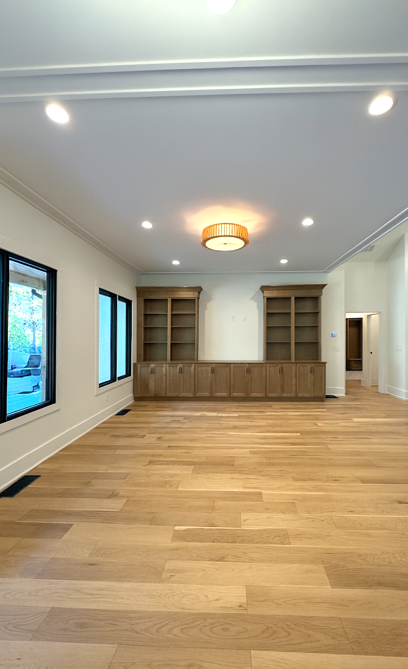 Empty room with wooden floors, built-in bookshelves, and recessed lighting.