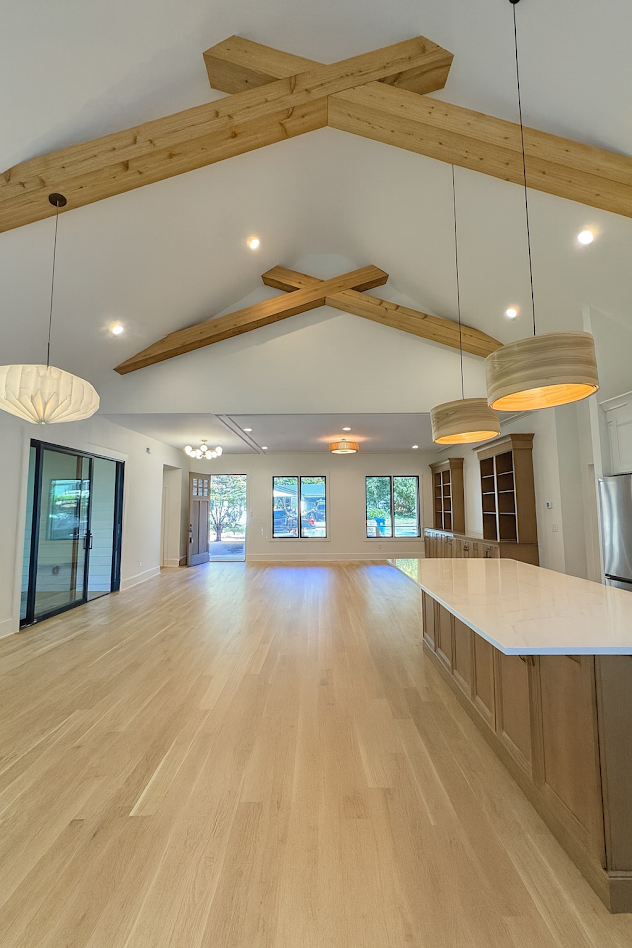 Light-filled open-plan living area with vaulted ceiling, exposed wooden beams, and pendant lights over a large island.