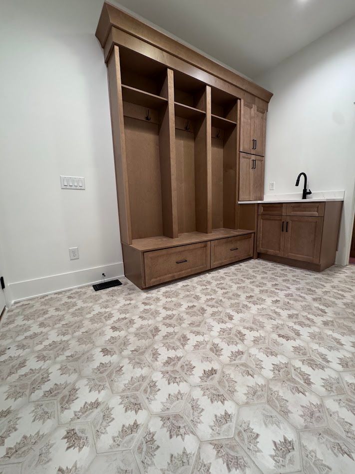 Mudroom with wooden lockers, bench, cabinets, and a sink. Tan and white patterned floor.