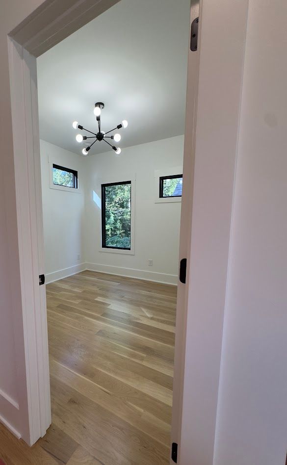 View through an open doorway into a room with wood floors, white walls, and a black chandelier.