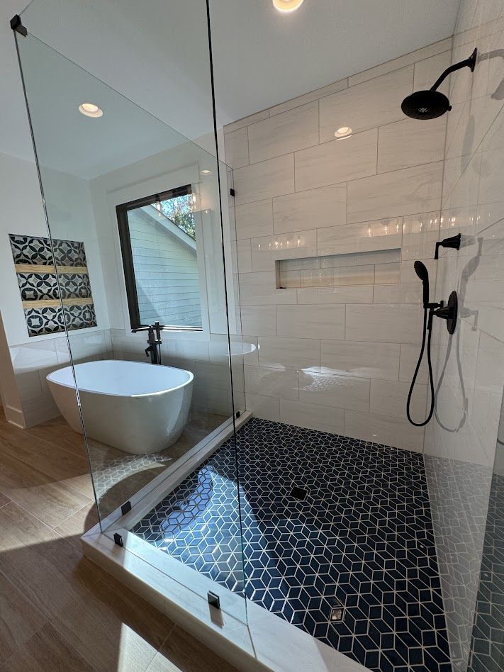 Modern bathroom with white and black tile, glass shower, freestanding tub, and black fixtures.