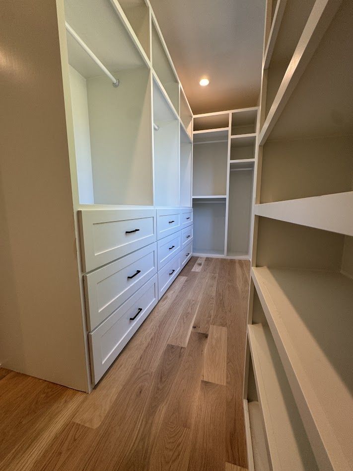 Walk-in closet with white shelves and drawers, wooden floors.