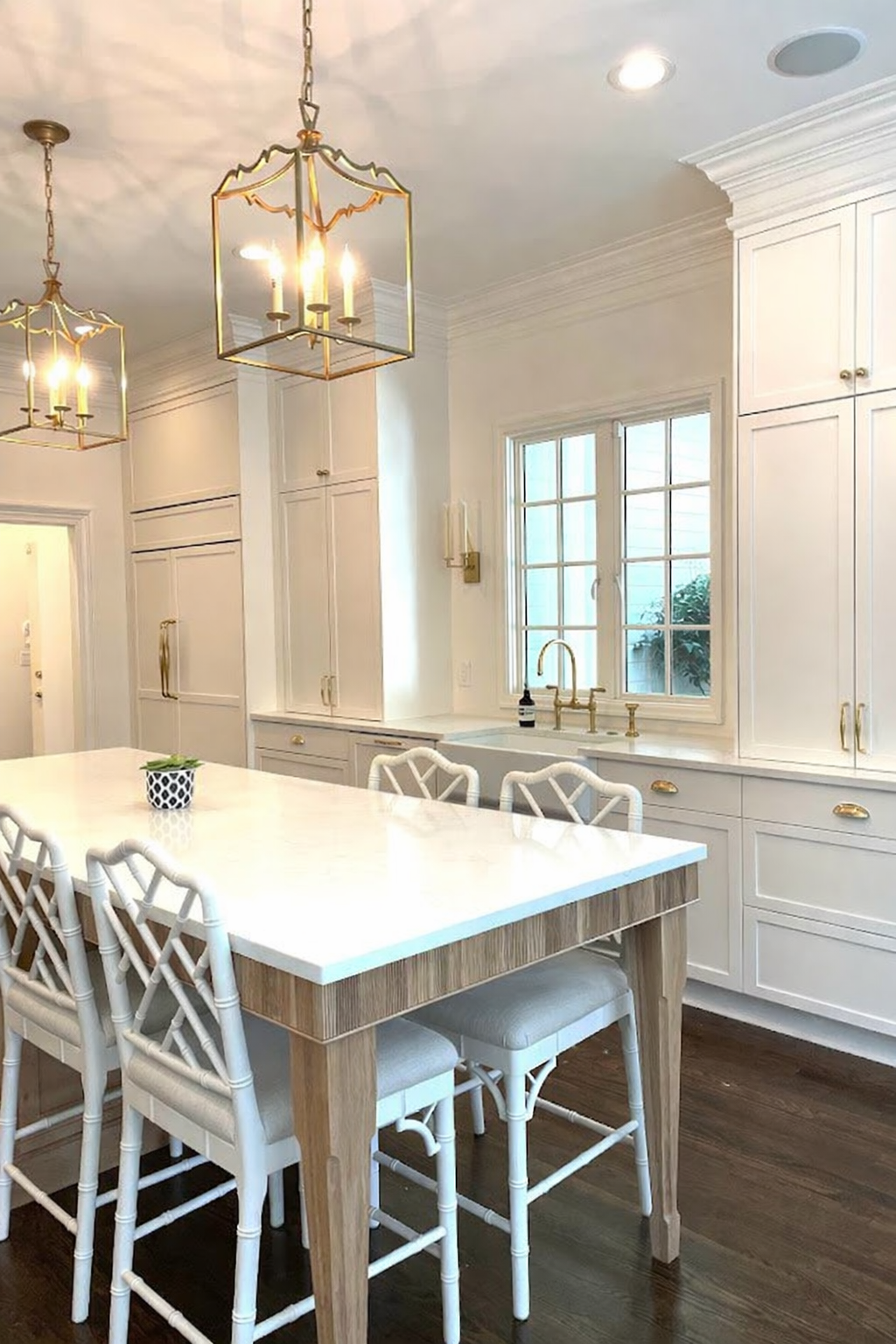Elegant white kitchen with marble-topped island, gold fixtures, and ornate pendant lights.